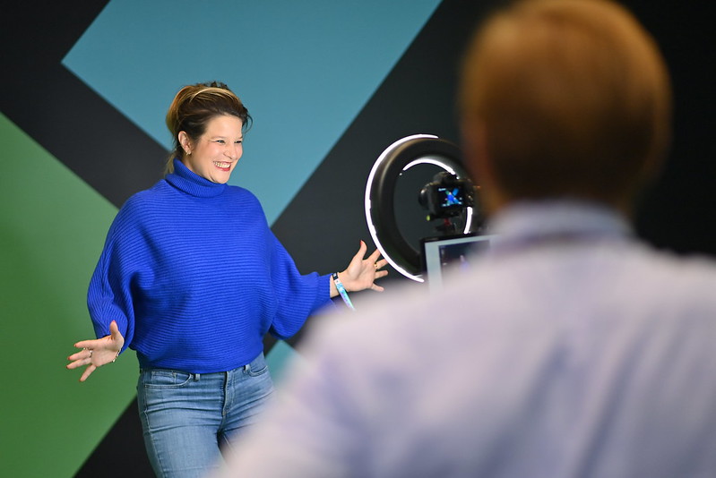 A young woman poses for a camera in front of a ring light, smiling widely